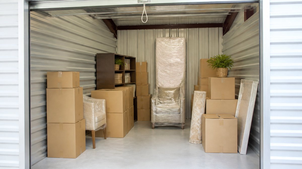 Clean, well-lit storage unit with stacked boxes and furniture covered in moving blankets